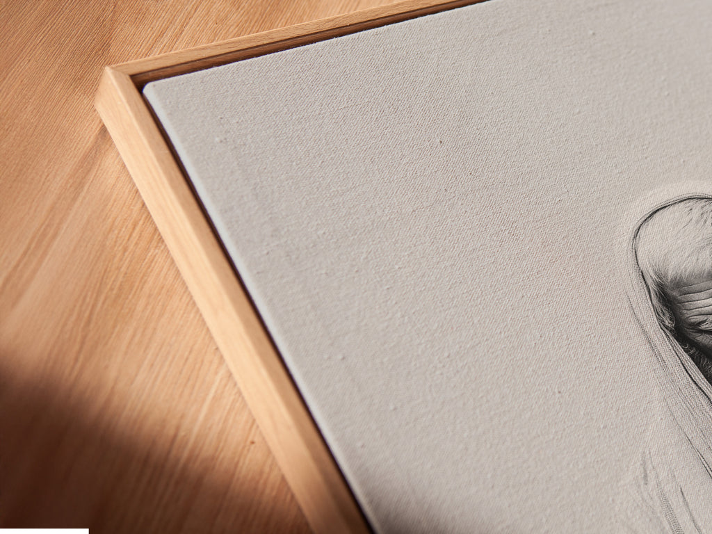A close-up angled view reveals a canvas print in a floating frame. The frame enhances the artwork. The art features a man holding a lamb. The details and texture of the canvas are visible. The floating frame adds dimension to the artwork.