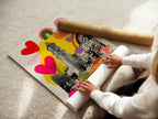 A woman carefully rolling a fine art poster paper. The paper features a clock tower.  It also has colorful hearts and rainbows. High-quality materials ensure the artwork lasts for years.  Perfect for art enthusiasts who appreciate fine details.  Explore our selection of premium art prints.