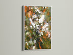 A white frame showcases abstract floral art. This piece features orange green and white colors. It offers a clean and contemporary look. It will brighten up any space. Perfect for minimalist or modern interiors. Add a splash of color to your walls.