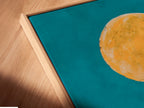 A close-up angled view reveals a canvas print in a floating frame. The Wolf Moon artwork is beautifully showcased. The teal and orange colors create a captivating scene. This southwestern desert wall art enhances any interior. It is a modern and stylish piece.