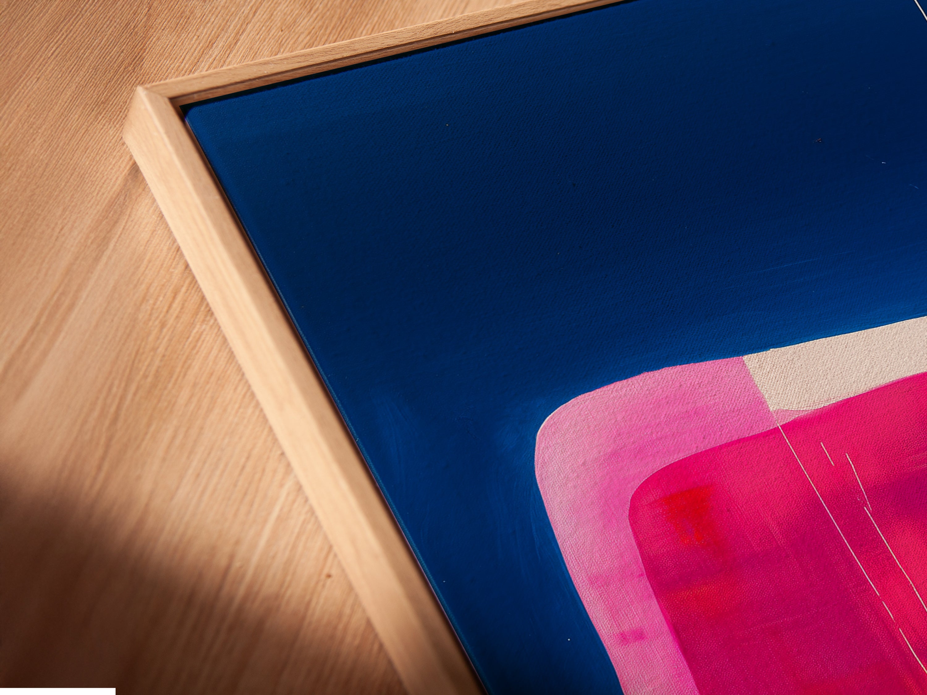 A close-up angled view reveals the texture of a canvas print in a floating frame. The abstract geometric artwork boasts blue orange and pink colors. The floating frame enhances the contemporary feel. A unique piece for modern art lovers