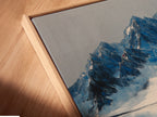 Angled close up of a mountain reflection canvas print in a floating frame.  The indigo blue lake wall art is perfect for modern office decor.  The floating frame enhances the landscape artwork. Its reflection print adds a touch of winter to any space. This is a great mountain painting.