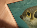 A close-up angled view reveals the canvas print in a floating frame. This otter family artwork adds charm to any room. Perfect for coastal decor or nursery art. The teal blue hues create a calming atmosphere and showcase the animal artwork.