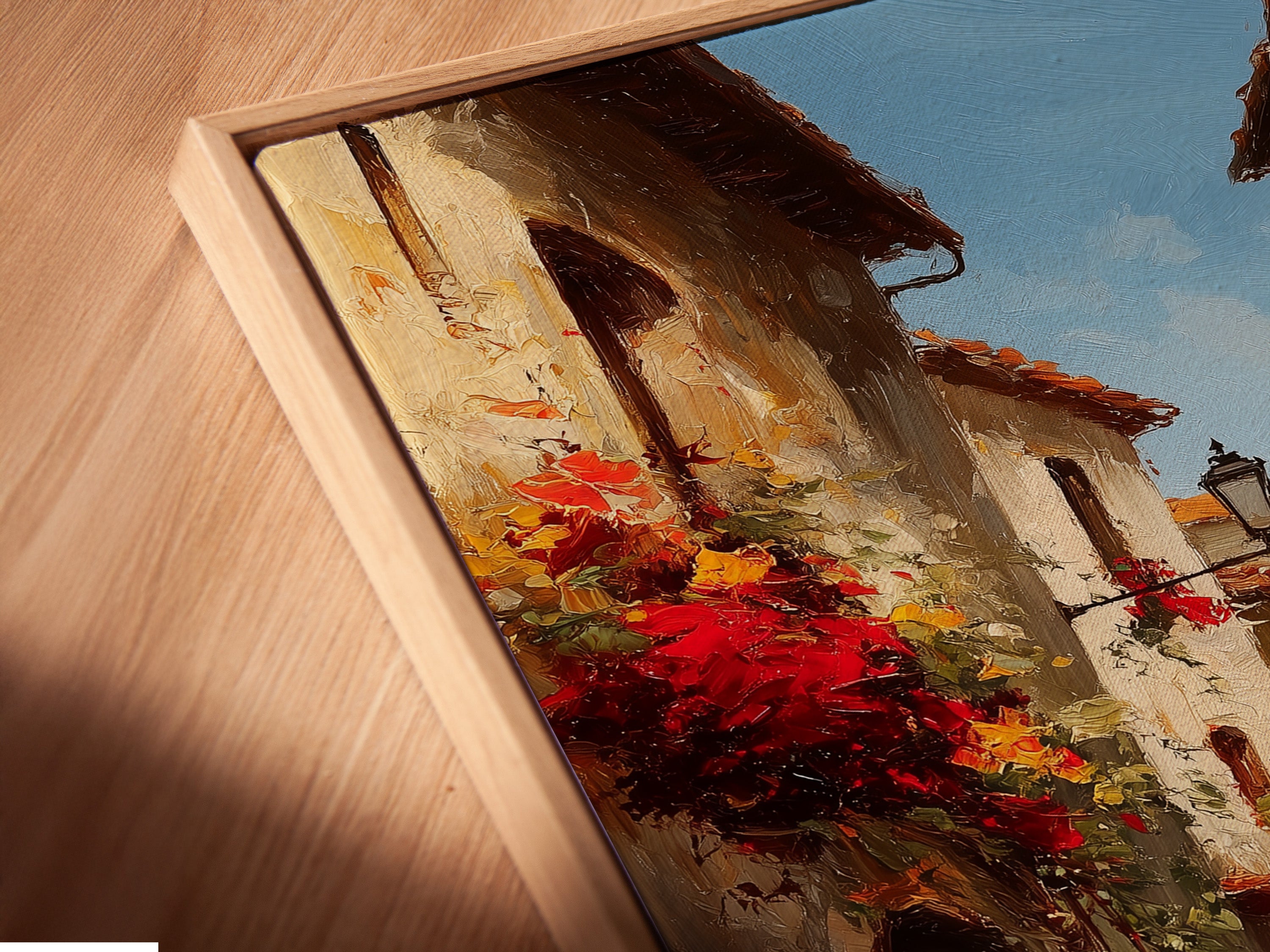 Angled close-up of a canvas print in a floating frame. The artwork is a detailed Italian street scene with red flowers. The floating frame adds a modern touch. The light emphasizes the texture and depth of the canvas print. It creates a gallery-like feel.