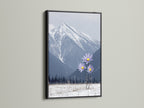 The mountain flower art is striking in a black frame. This winter landscape wall art features snowy mountains and vibrant lilac flowers. It is ideal for bedroom decor. Nature photography meets modern style in this unique piece.