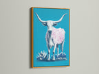 Longhorn cow artwork presented in a gold frame. The artwork features a turquoise background. A cow with pink spots stands out. The gold frame adds a touch of elegance. It is ideal for eclectic or bohemian decor settings.