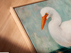 A close-up angle captures the canvas print in a floating frame. Notice the fine details of this coastal bird wall art. The floating frame adds depth to the artwork. This teal and white artwork is perfect for bathroom wall decor. The Egret art is a serene addition to any space. Discover the beauty of this heron print today.