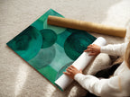 A woman carefully rolls fine art poster paper. The emerald green abstract art will soon become a modern masterpiece. The geometric circle artwork is ready for display. This artwork is perfect for art enthusiasts.