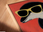 Angled close up reveals a canvas print of a retro penguin artwork in a floating frame. The quirky bird art is perfect for kids room decor or a unique wall display. Sunglasses art stands out against a red backdrop. The floating frame adds a modern touch. It enhances the playful art print making it a fun addition to any room.