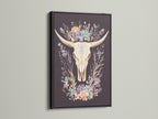 Artwork featuring a bovine skull with floral elements. It is encased in a black frame. The black frame provides a bold and contemporary look. The artwork makes a statement on any wall. A striking contrast is created with lighter backgrounds. This art piece adds drama to your space.