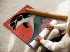 A woman rolls a fine art poster paper of a retro penguin artwork. This cool animal print is ideal for creating playful kids room decor. The quirky bird art features sunglasses against a red backdrop. This high quality poster paper ensures a vibrant and long lasting display. Perfect for adding a fun touch to any space with this colorful bird art.
