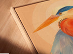 Angled close up of a canvas print in a floating frame. The heron artwork is displayed in a modern coastal setting. The blue and orange hues of the bird canvas print add vibrancy to any room. The floating frame enhances the modern art print. Perfect for adding a nature inspired touch to your office wall decor.