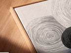 A close-up of a canvas print. The abstract geometric art features black and white circles. It is set in a floating frame. The angled view highlights the texture and depth. This is ideal for modern minimalist spaces adding a touch of elegance.