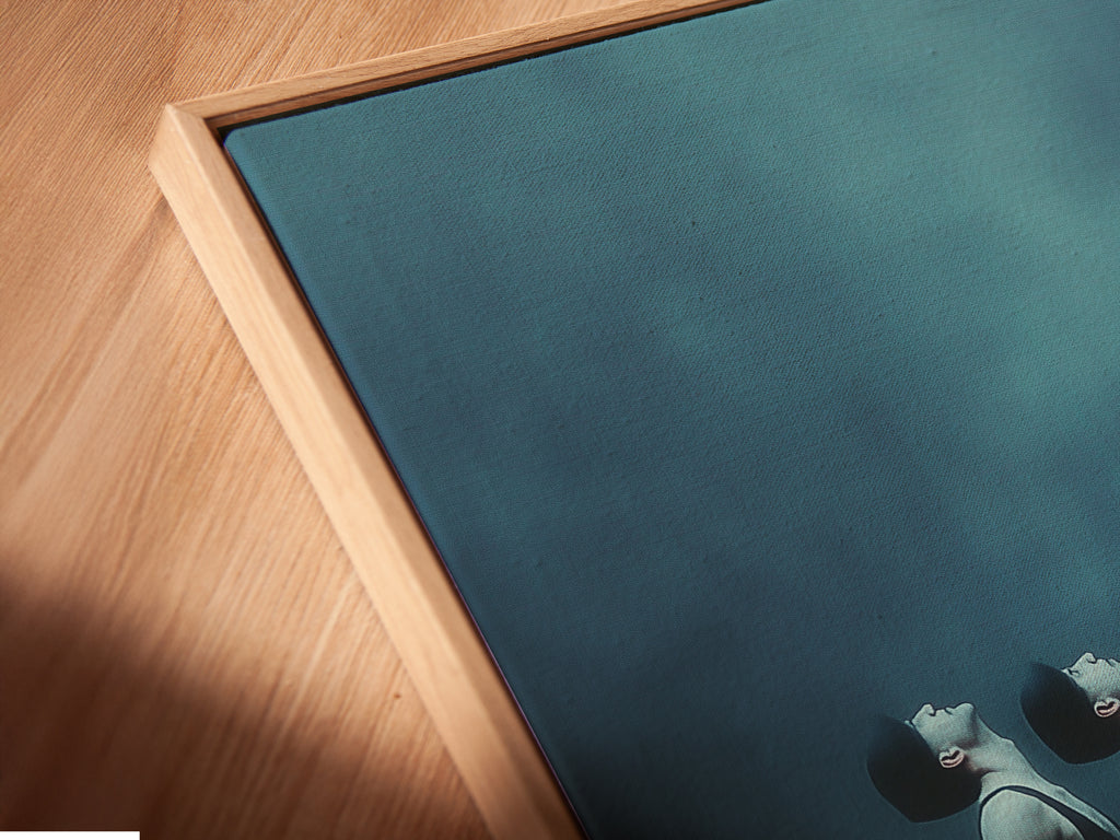 A close-up angled view reveals a canvas print in a floating frame. The teal and blue tones of the surreal figures artwork are highlighted. This display emphasizes the modern and ethereal qualities of the piece. It is perfect for creating a serene atmosphere.