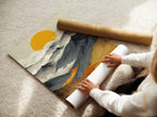 A woman is carefully rolling a fine art poster paper. She's handling a mountain sunrise landscape. The poster showcases abstract nature art. Perfect for those who appreciate golden sun decor. Get ready to display this warm tone print in your home. Fine art paper ensures a high-quality print.