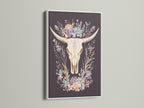 Artwork featuring a bovine skull with floral elements. It is encased in a white frame. The white frame offers a clean and modern aesthetic. It allows the artwork to stand out. The art piece is perfect for light-colored walls. Consider this art piece for a sophisticated look.