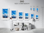 A size comparison chart in an interior setting. The chart shows various sizes of mountain view artwork. Available options include canvas and framed prints. The artwork has a bright blue sky and a snow-capped mountain.
