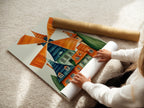 A woman carefully rolling a fine art poster paper print. Featuring whimsical windmill artwork. This Dutch architecture piece is perfect for playroom decor. Explore colorful folk art for kids' rooms and creative spaces.