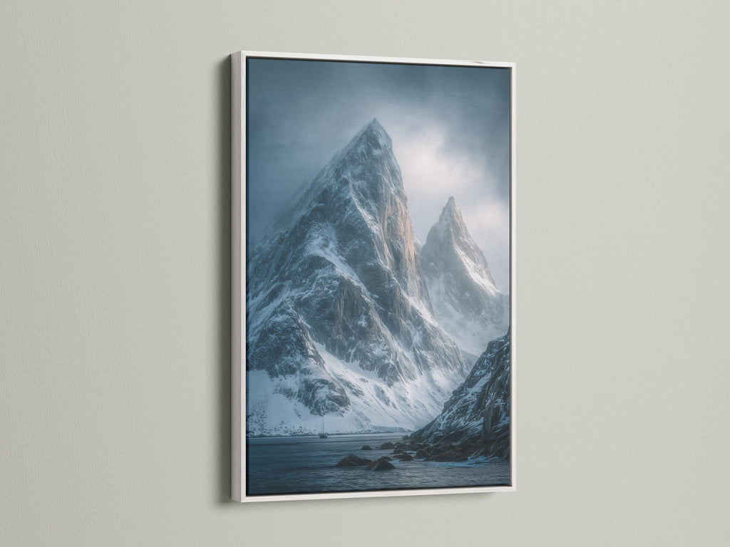 A white frame highlights a blue gray art print of a snowy mountain range. This moody landscape poster adds winter scenery to any room. Discover this stunning piece of Scandinavian art.