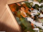 A close-up shot shows a canvas print in a floating frame. The abstract floral art has orange green and white colors. The floating frame adds depth and sophistication. Perfect for adding a gallery-like touch to your home. This artwork is a modern masterpiece.