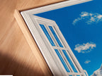 A close-up of a canvas print in a floating frame. The artwork showcases a mountain view. The print features a bright blue sky with fluffy clouds. A snow-capped mountain is seen through an open window. This artwork is modern. 