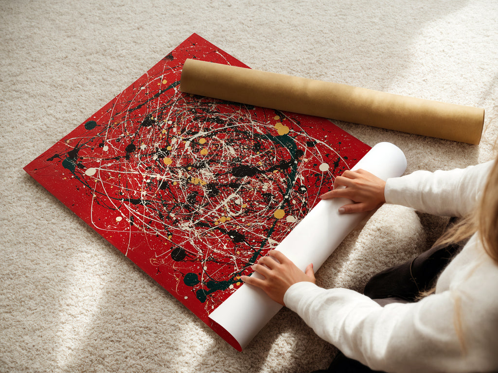 A woman carefully rolls a fine art poster paper. The paper features abstract splatter art. This red canvas wall art is perfect for modern decor. The paint drip artwork adds a contemporary touch. Ideal for creative spaces and modern homes. Enhance your collection with this expressive piece.