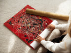 A woman carefully rolls a fine art poster paper. The paper features abstract splatter art. This red canvas wall art is perfect for modern decor. The paint drip artwork adds a contemporary touch. Ideal for creative spaces and modern homes. Enhance your collection with this expressive piece.