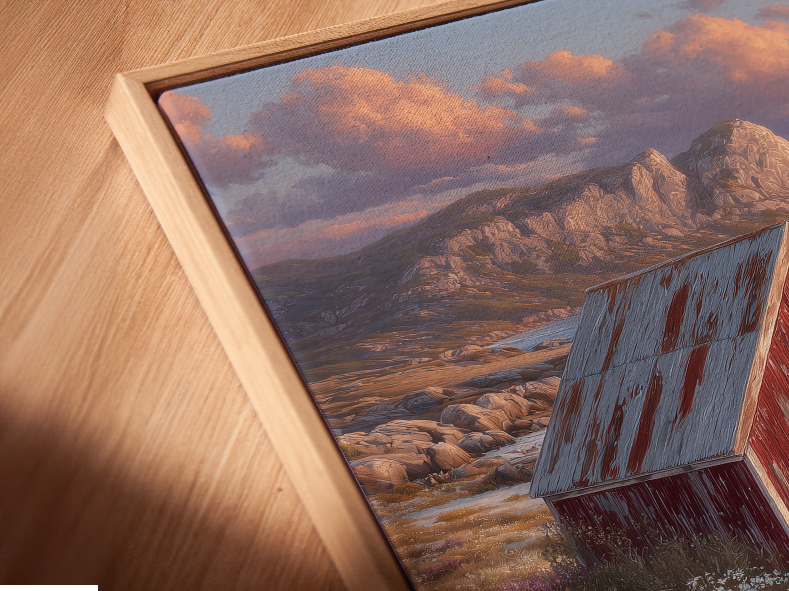 A close-up angled view of a canvas print in a floating frame. The artwork depicts a coastal cottage scene. It features a rustic red barn and seaside landscape. Perfect for adding a touch of countryside charm.