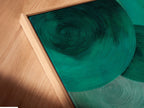 A close-up shows a canvas print in a floating frame. The emerald green abstract art is a modern geometric circle. This contemporary artwork appears elegant and stylish. Ideal for contemporary print collectors.