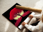 A woman is carefully rolling a fine art poster paper of the Crimson Tree artwork. The red cityscape wall art is a modern silhouette. This fine art poster paper ensures quality and detail. Perfect for preserving your modern art.