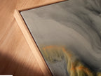 Angled close up of a canvas print in a floating frame. The artwork features a topographical map. The floating frame adds depth. It creates a modern aesthetic. This view highlights the texture. It shows the quality of the print.