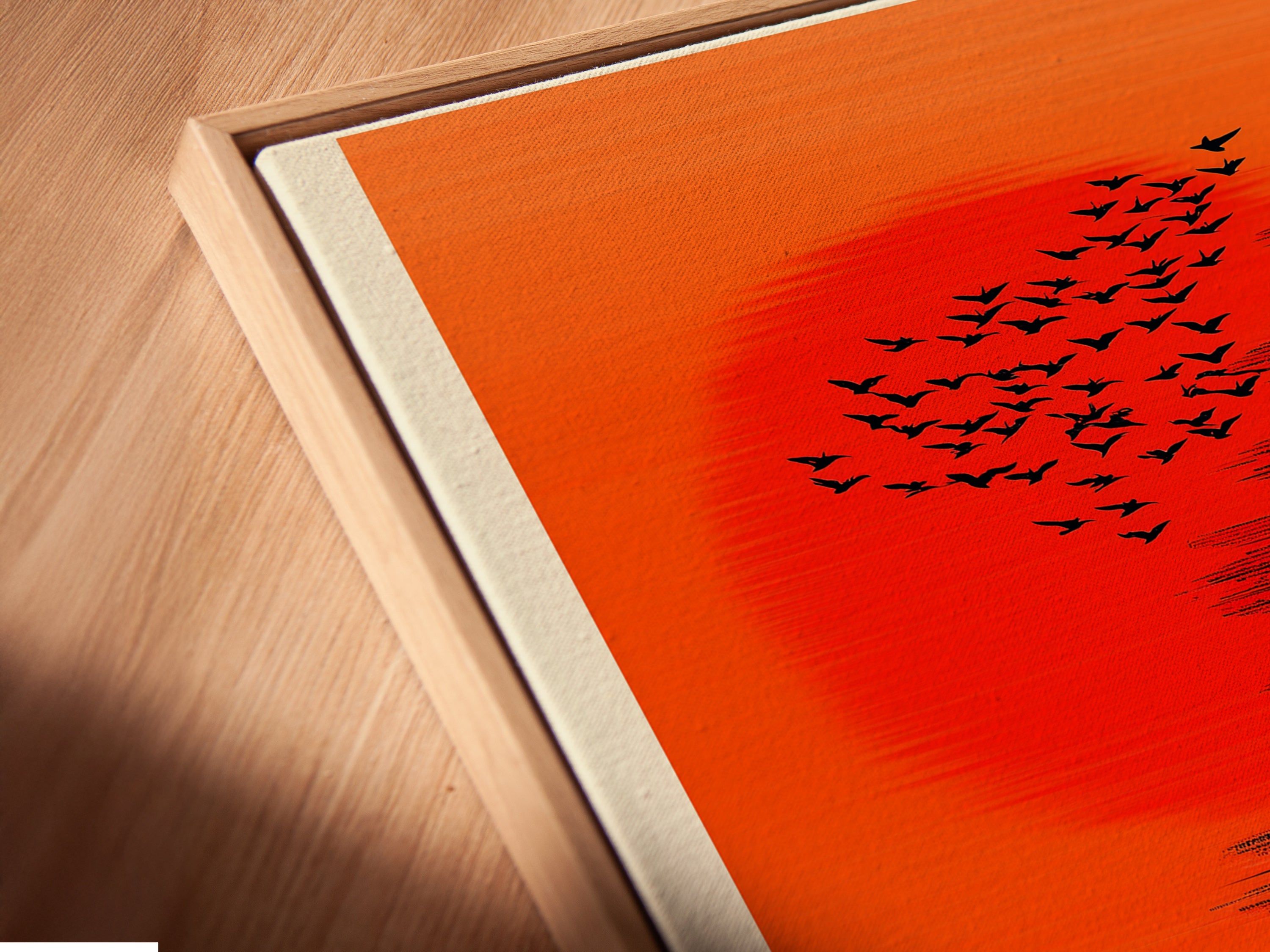 Angled close up of a canvas print in a floating frame. This abstract wall art features birds and people under an orange sky. Perfect for modern decor. It's a unique piece to enhance any room's aesthetic appeal.