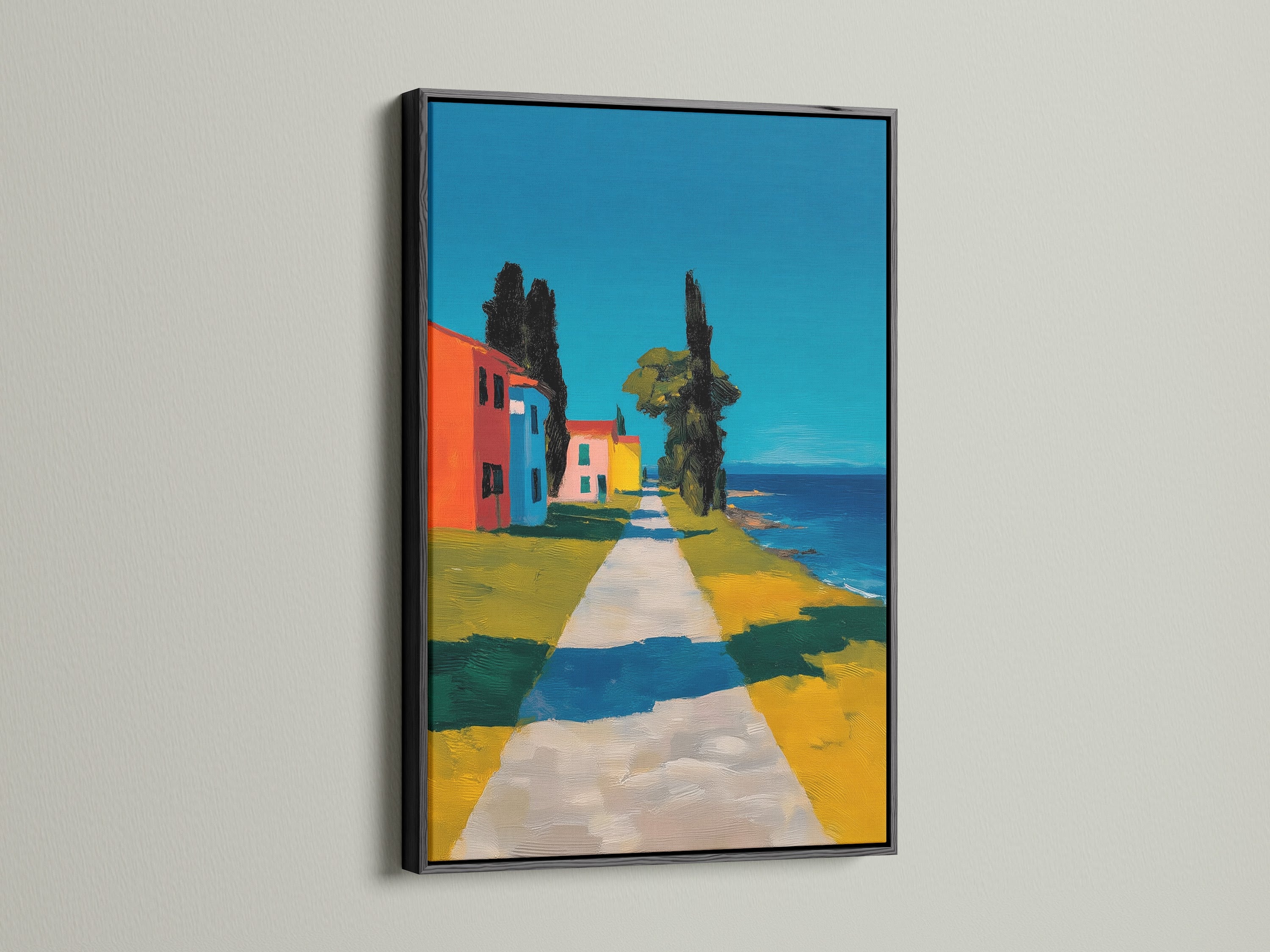 Artwork with a black frame is displayed. The art features a path leading to colorful buildings. It is a coastal scene under a bright sky. The black frame provides a bold contrast. It emphasizes the artwork's details.