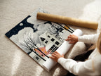 A woman carefully rolls a fine art poster paper of Winter Village art. This snowy night art is perfect for adding a Scandinavian touch to your decor. Bring a cozy winter landscape into your home.