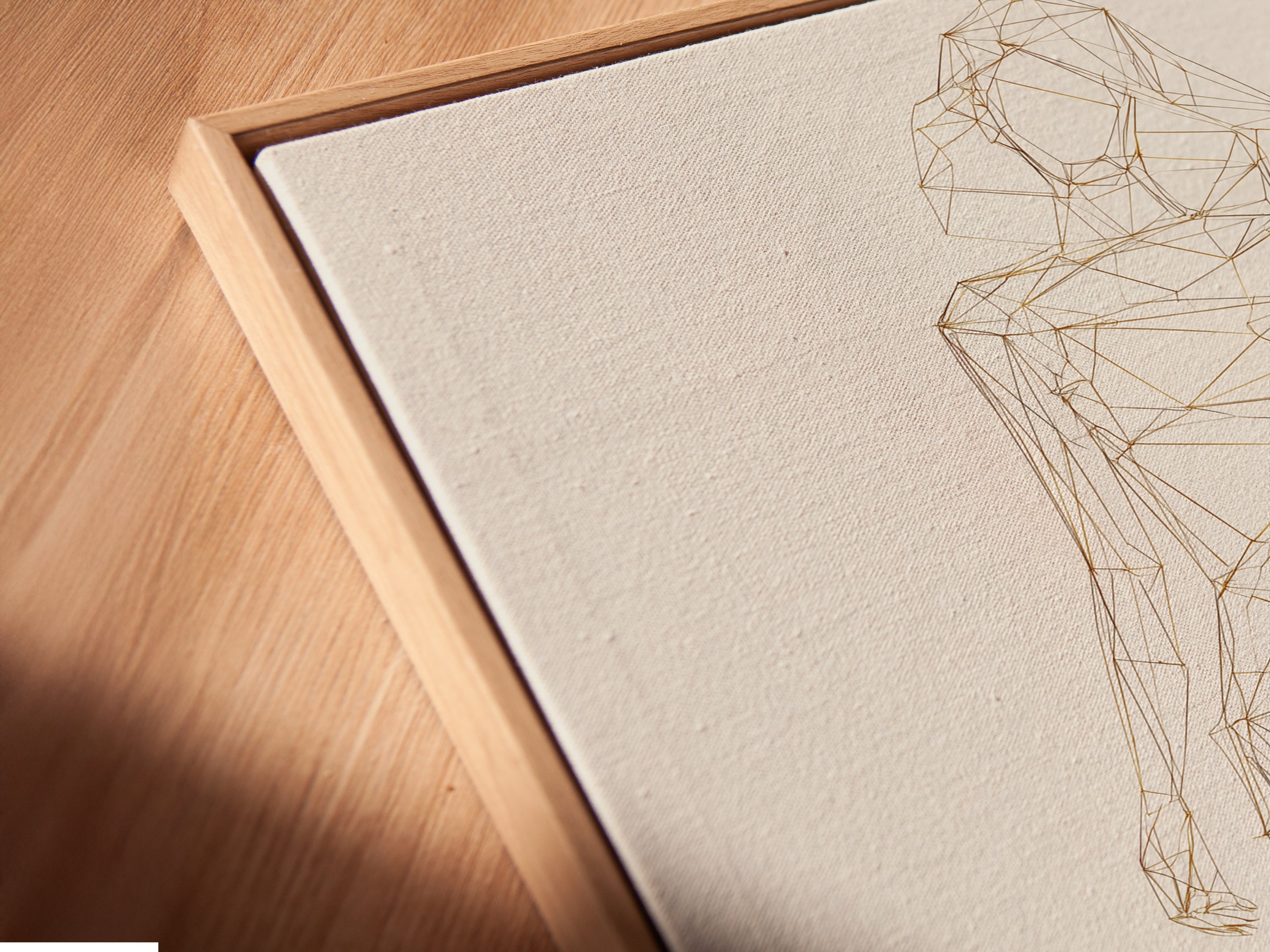 A close-up angled view of a Geometric Woman canvas print. It's displayed in a floating frame. This minimalist line drawing is modern fashion sketch artwork. The beige and gold colors are beautiful. Enhance your space with this refined contemporary wall decor. Ideal for minimalist modern or Scandinavian aesthetics