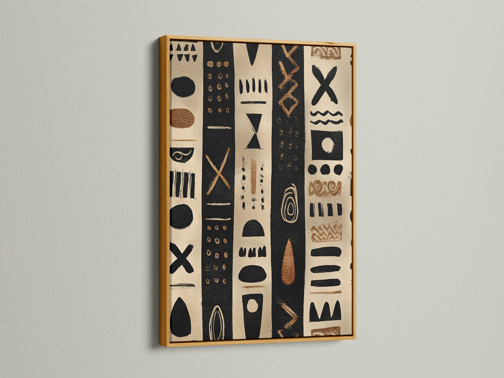 Artwork in a gold frame. The artwork has black and tan stripes with tribal inspired shapes. The artwork is hanging on a white wall. The gold frame adds a touch of luxury. This artwork is perfect for modern and classic homes.