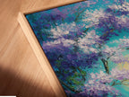 Close-up angled view of a canvas print in a floating frame. The floating frame gives the artwork a contemporary look. This art piece features an abstract tree with purple leaves and blue water. The frame enhances the overall aesthetic of the artwork.