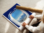 A woman is carefully rolling a fine art poster paper. The paper features an airplane window view with a scenic mountain landscape. High-quality fine art poster for travel enthusiasts. Perfect for modern wall art.