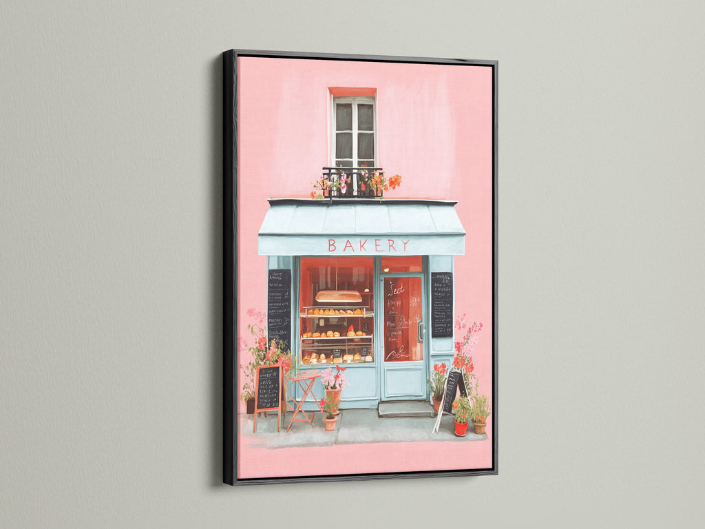 Artwork presented in a black frame. The art captures a bakery storefront with pink walls and a blue awning. The black frame offers a bold and sophisticated contrast. This piece is perfect for adding a stylish statement to your home decor with its striking presence.