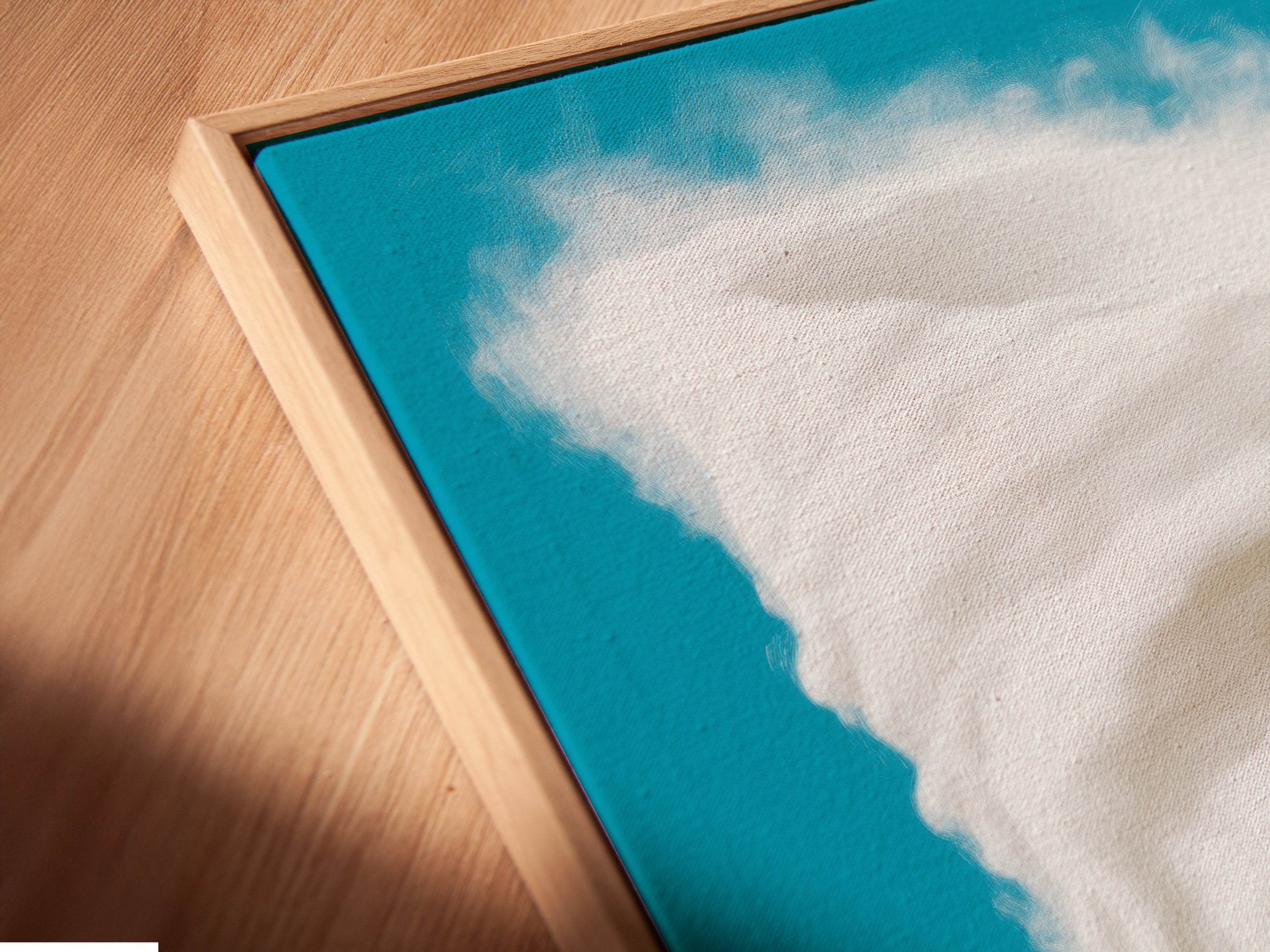 A close-up angled view reveals the intricate details of a canvas print in a floating frame. This modern wall art showcases a surreal coffee cup storm. The turquoise sky and fantasy beach art enhance home decor. Perfect for adding an imaginative touch to any room.