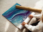 A woman is carefully rolling a fine art poster paper. She is preparing an ocean wave abstract artwork. This teal and purple fluid art will become coastal wall art. Ideal for bedroom decor.