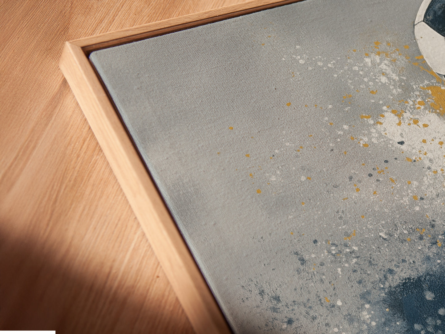 A close up shows a canvas print in a floating frame. The soccer artwork features abstract blue and gold details. It is perfect for adding a modern touch to any room. The floating frame enhances the artwork. Consider this for your sports themed decor.