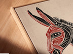 Angled close-up of a canvas print in a floating frame. The Tribal Donkey art is displayed. The floating frame enhances the artwork's contemporary appeal. This southwestern animal artwork is ready to hang. The red and black art makes a statement. Ideal for modern office wall decor.