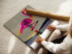 A woman is carefully unrolling a fine art poster paper print. The paper showcases a flamingo balancing on a zen stone stack. This high-quality print is perfect for framing. It brings a touch of zen and tropical charm to your home.