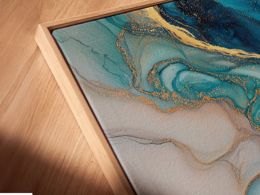 A close-up angled view reveals the intricate details of a canvas print in a floating frame. The blue abstract art features fluid acrylic textures and gold accents. This piece adds a modern coastal touch to any living space. The artwork enhances modern bedroom decor with its teal and marble print.