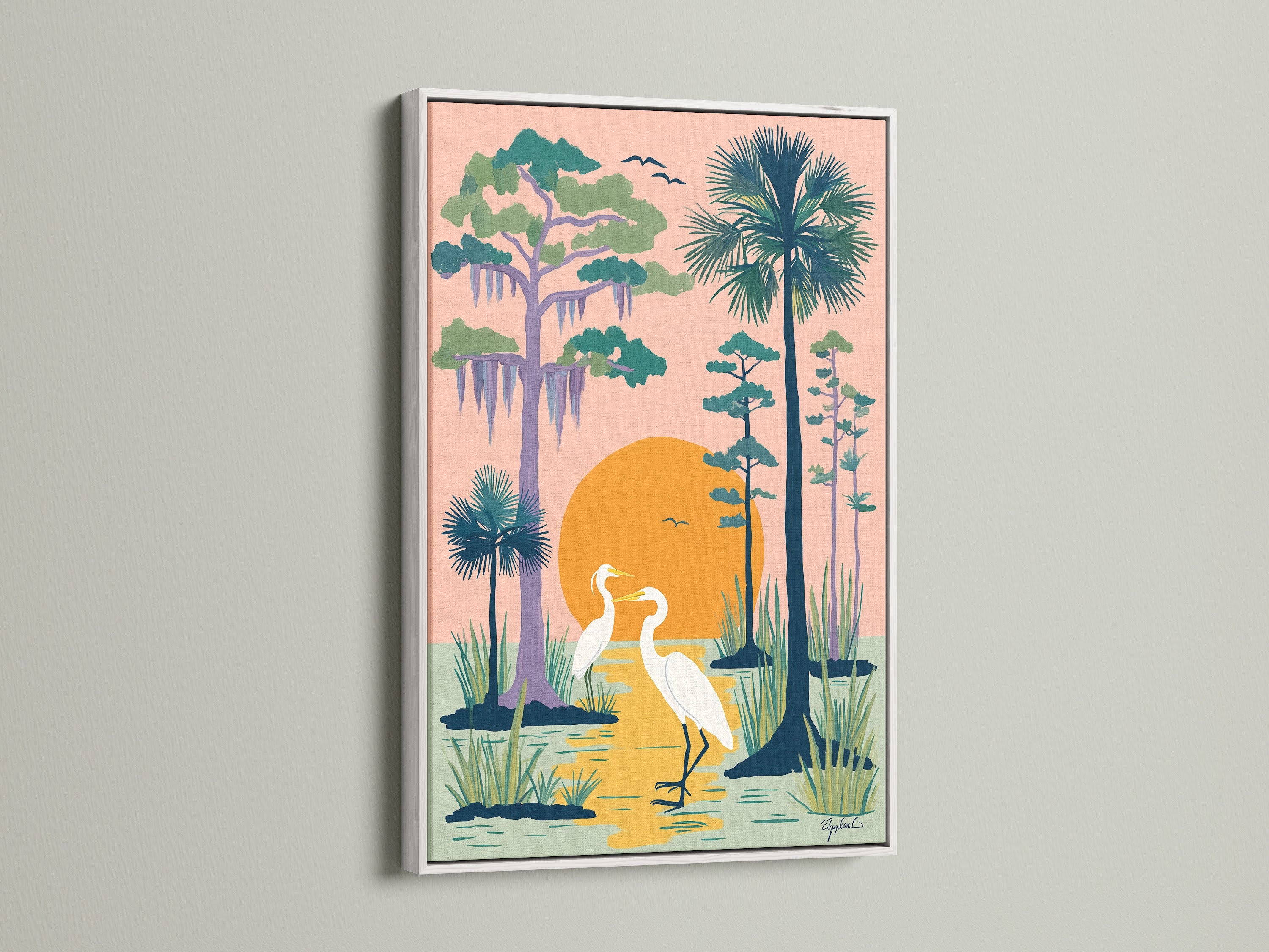 A heron artwork in a white frame hangs on a white wall. The coastal wall art depicts two herons in a peach swamp. The Florida landscape artwork complements any beach house. Perfect nature art print to brighten your living room.