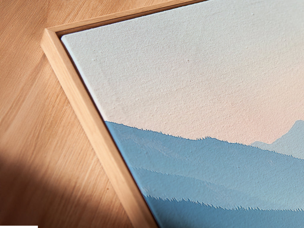 Angled close up of a canvas print in a floating frame. Pastel blue wall art is visible. The mountain lake artwork brings a serene touch. It is a calming nature landscape photography piece. Ideal for bedroom wall decor. The floating frame adds a modern touch. Enhances contemporary spaces.