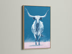 The longhorn bull artwork is showcased in an oak frame. The artwork is a western wall art piece. The blue and pink hues add a modern farmhouse touch. This bull canvas print is perfect for ranch decor.
