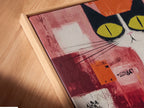A close-up shows a canvas print of Abstract Cat art in a floating frame. The modern animal poster brings a playful touch to any room. See the green and orange details in this unique folk art piece. Perfect for cat lovers.
