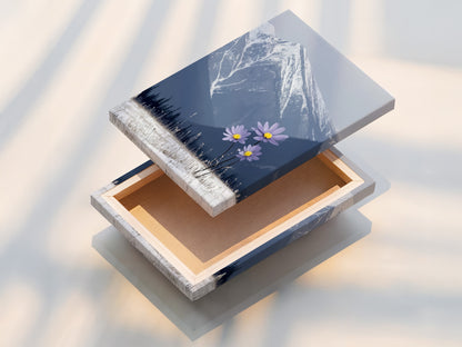 A stretched canvas print of mountain flower art is displayed. This winter landscape piece features snowy mountains and lilac flowers. It is a perfect modern addition to any wall. Nature photography and floral elegance combine beautifully.